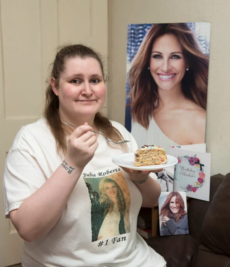 Lady holding cake with a photo of Julia Roberts on her t shirt and a poster of Julia Roberts in the background